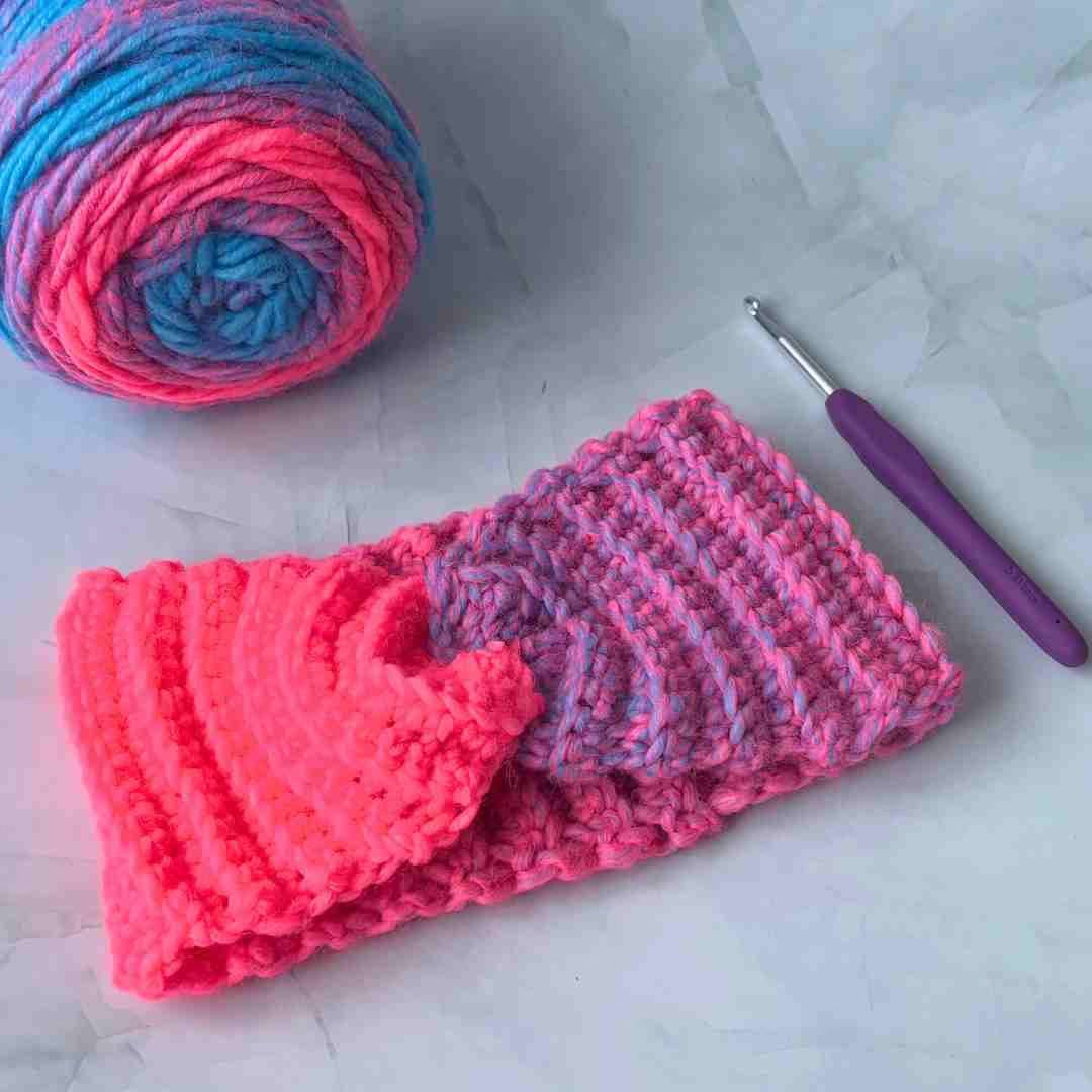 pink twist headband laying on display with crochet hook and yarn